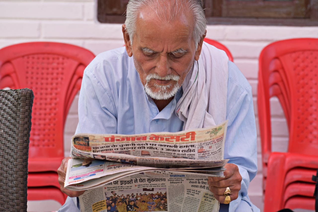 Elderly man engaging in daily reading of a newspaper while seated outdoors.