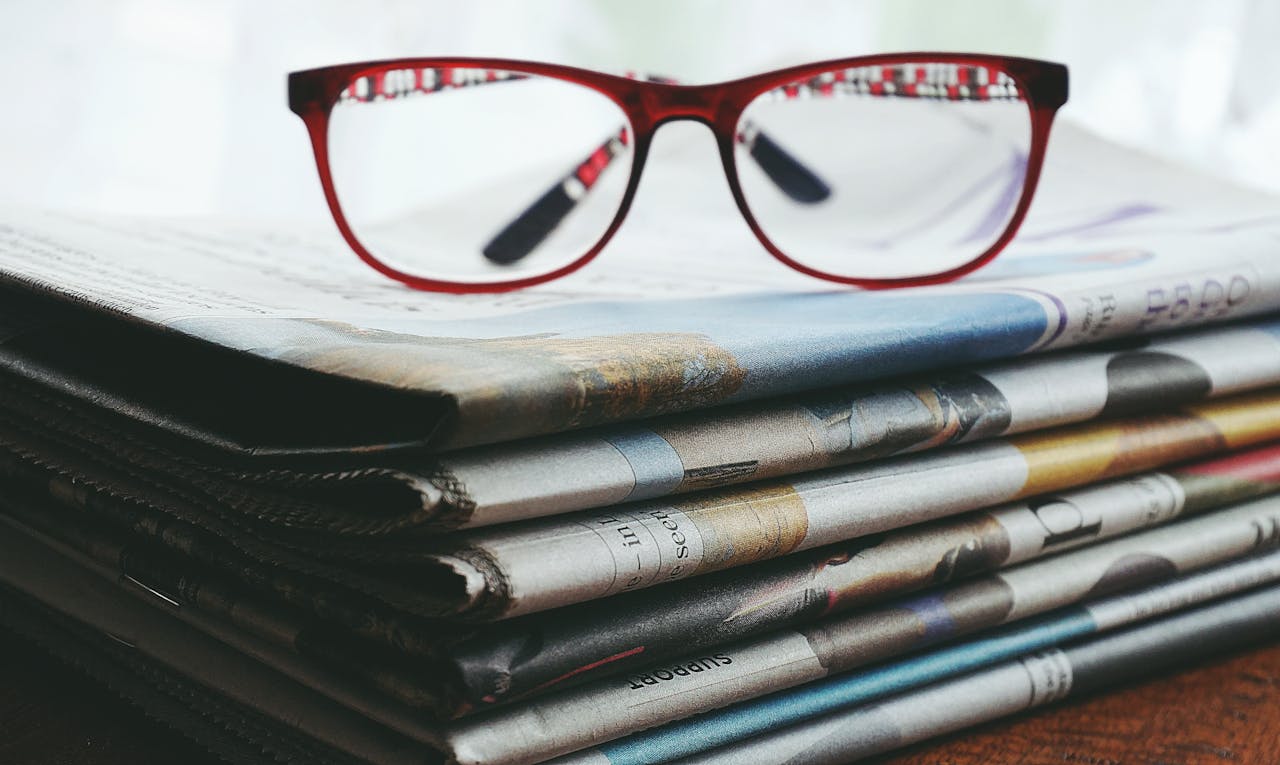 services-04 Red eyeglasses resting on a stack of newspapers symbolize reading and information.